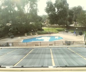 Multiple solar pool heater panels installed on a roof with the pool in the background.