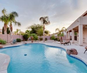 A large pool in the backyard of a home, with palm trees in the background.