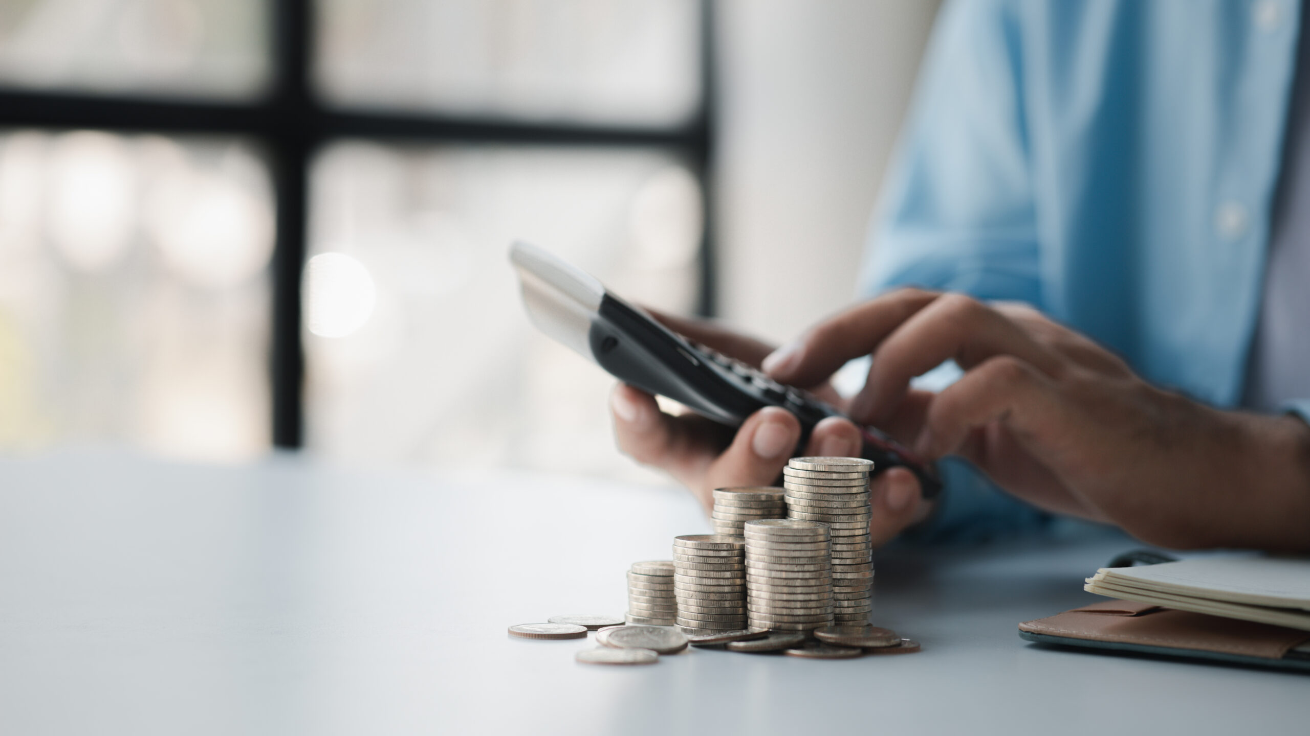 Person with stack of coins, saving money concept for future use Metallic coins stacked on a desk beside a handheld calculator, illustrating cost considerations for Celestial Solar & Water Systems, Inc. and solar thermal panels.
