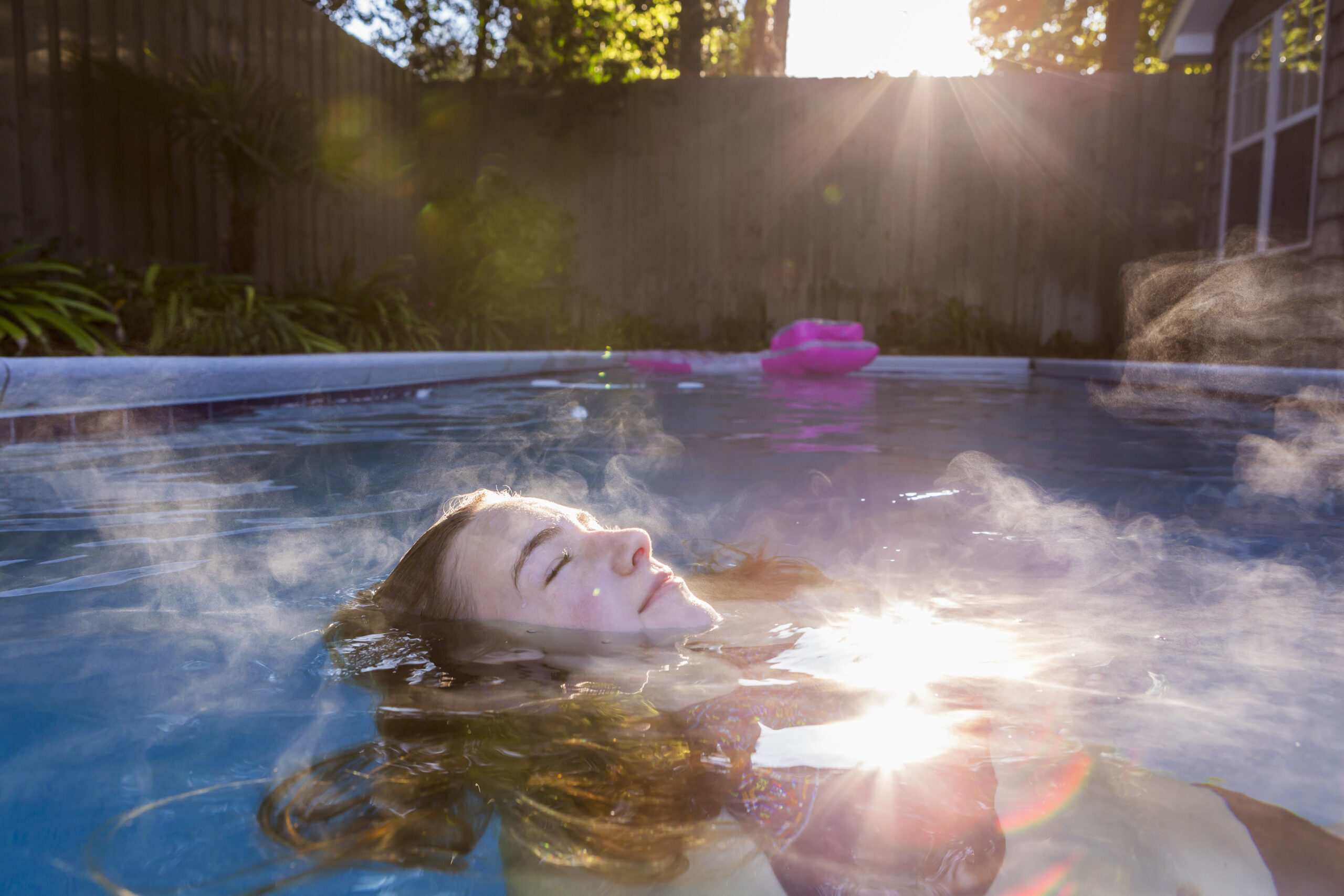 13 year old girl swimming in a pool Celestial Solar & Water Systems, Inc. sunlit pool scene with a swimmer in a blue backyard pool, warm sun rays and a pink float in the background