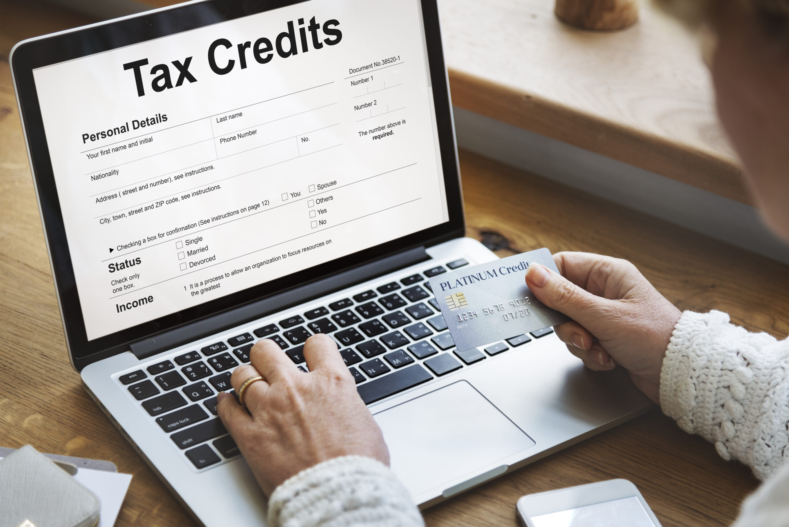 Tax Credits Claim Return Deduction Refund Concept White laptop screen displays 'Tax Credits' form, while a blue Platinum card is held near the keyboard, reflecting solar tax credits context for Celestial Solar & Water Systems.