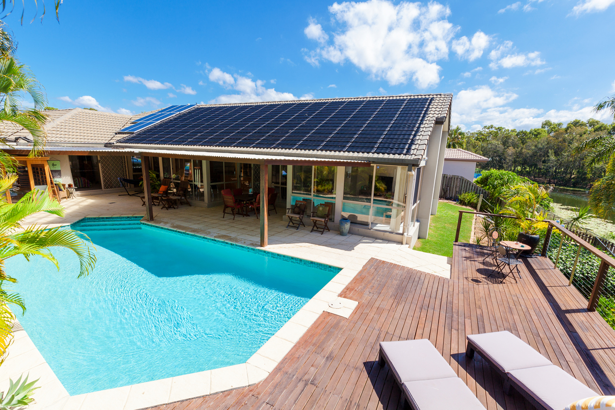 Backyard with swimming pool Sunny San Diego backyard with solar panels on a tiled roof, a bright blue pool, and a wooden deck, highlighting Celestial Solar & Water Systems, Inc. energy efficiency.