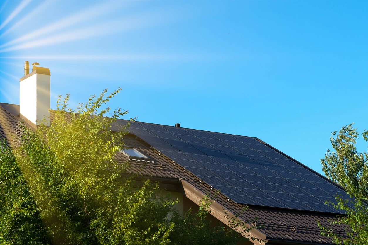 Solar electric panels on the roof of the building. Green energy in the house. Celestial Solar & Water Systems, Inc. rooftop solar panels gleam under a blue sky, highlighting a solar installation on a residential roof with lush green trees nearby.