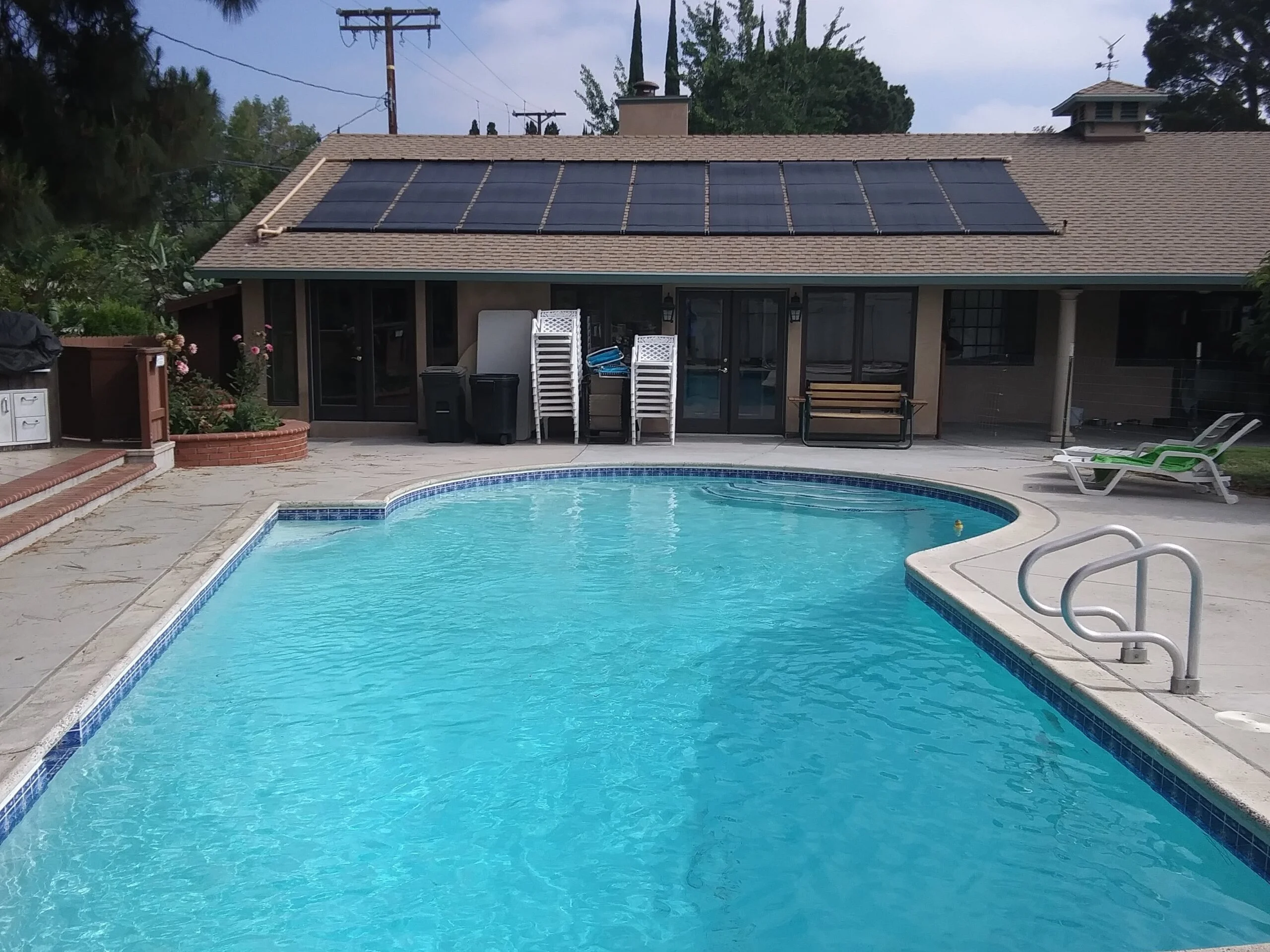 Winter Solar Pool Heating Installations Celestial Solar & Water Systems, Inc. rooftop solar panels on a tan house overlook a bright blue rectangular pool with a surrounding patio and lounge area.