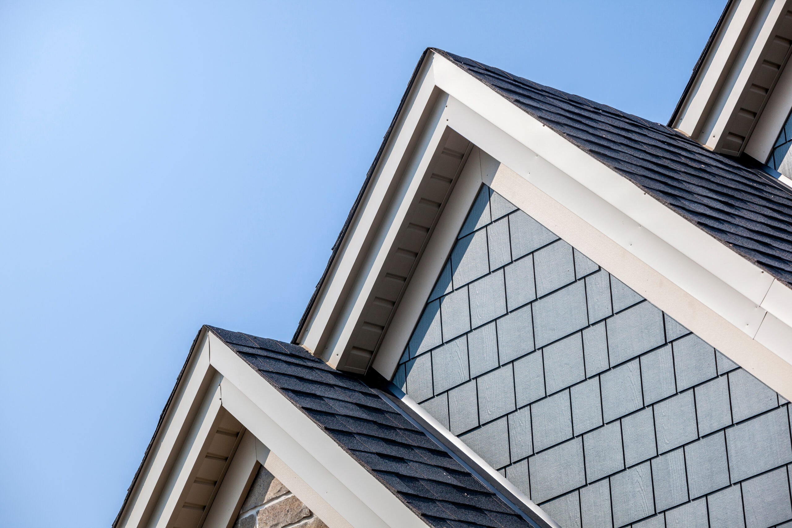 House Roof Celestial Solar & Water Systems, Inc. roofline showing a sloped dark asphalt shingle roof with white fascia and blue-gray siding, under a clear sky
