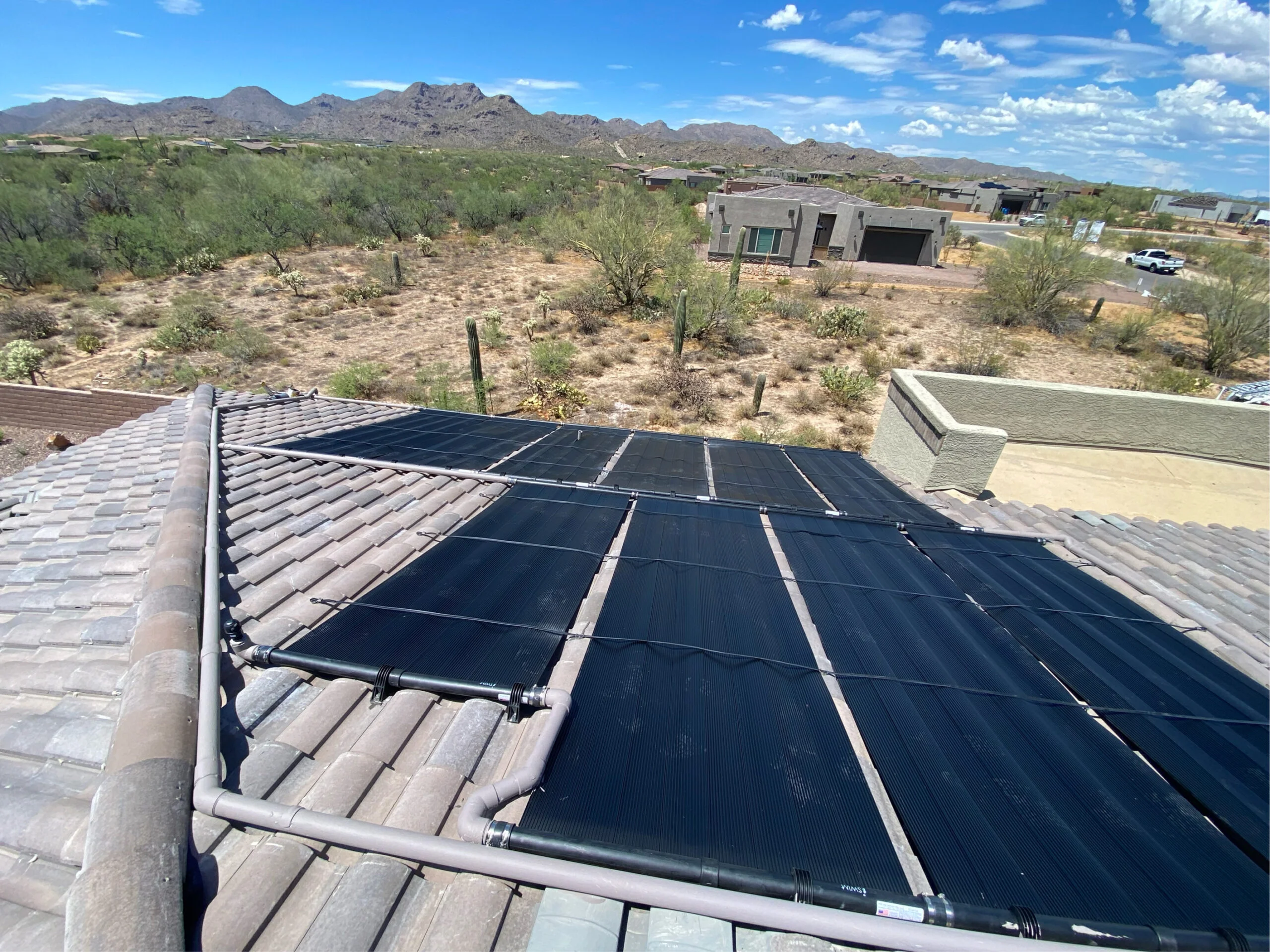 ios_48000EE7-6D6C-4D7C-A23D-3A09D330C58E Desert rooftop with dark solar panels installed over clay tiles, overlooking cacti and distant mountains near Las Vegas, Arizona; rooftop solar array on a sunny day.