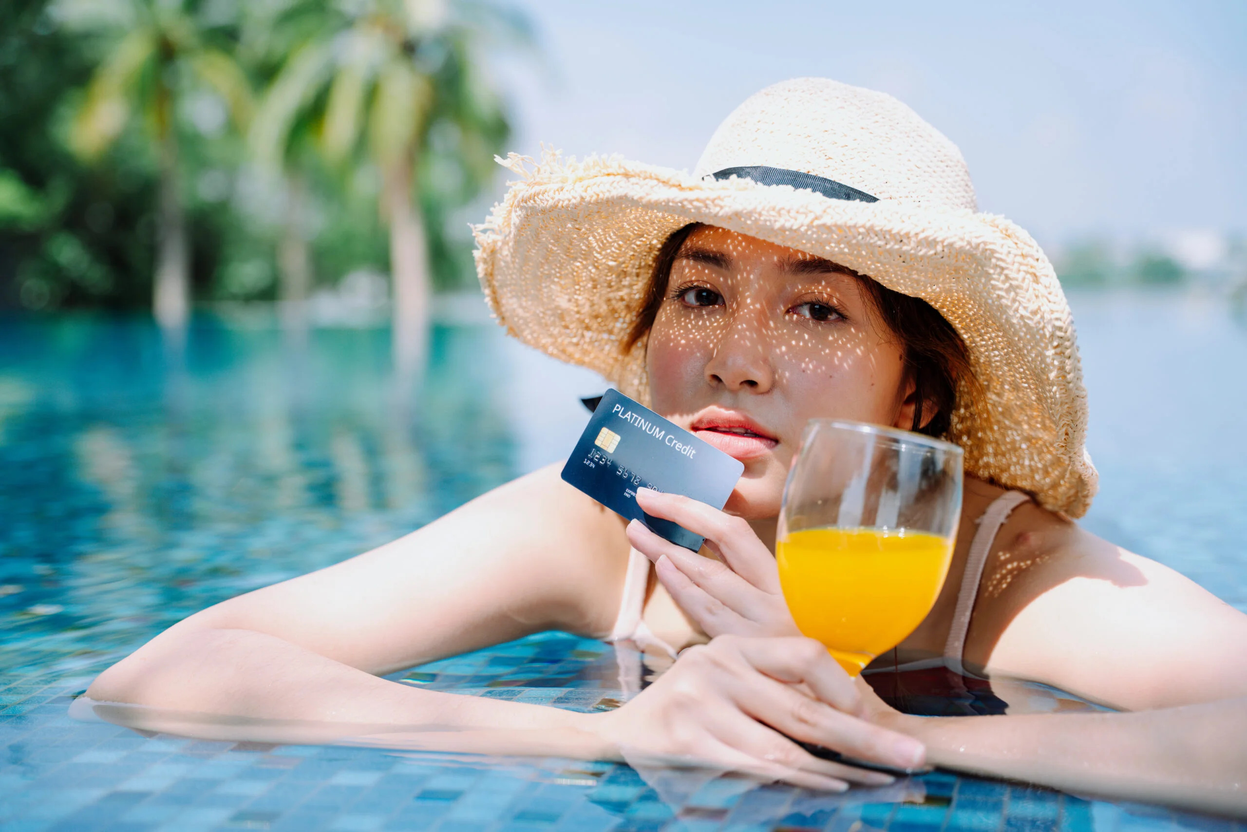 Sunlit poolside scene with a swimmer in a straw hat holding a credit card and drink, reflecting solar pool heating cost concerns in 2026.