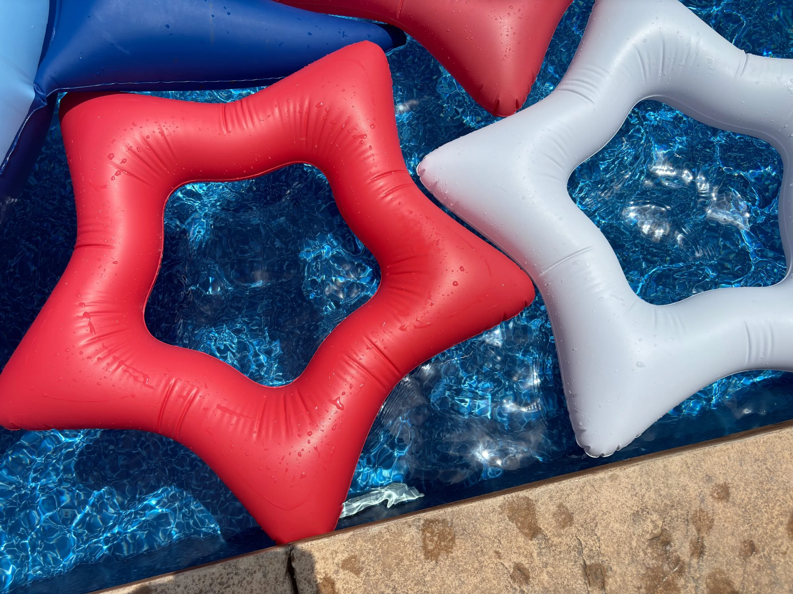 Memorial Day: red, white and blue inflatable pool floats with water droplets on clear blue pool water in warm May, ready to swim.