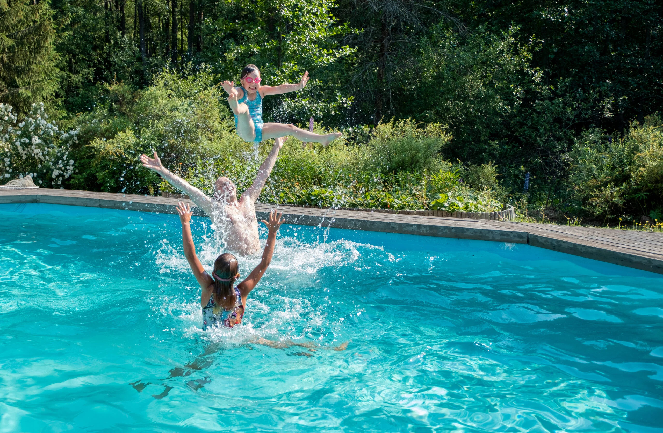 Caucasian girls 5 years old and their middle-aged father happily splash and dive in the outdoor pool. Summer vacation in the backyard of the cottage. Two swimmers leap into a sunny backyard pool, illustrating an extended swimming season with solar pool heating in September.